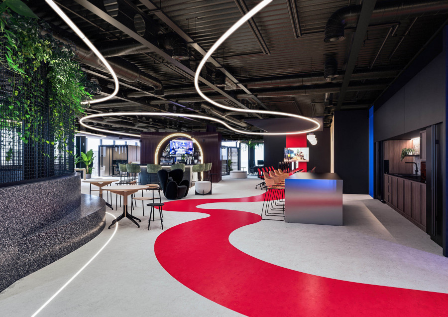 CGI showing an open-plan office with fluid red floor pathways, suspended curving LED lights, and mixed seating zones.